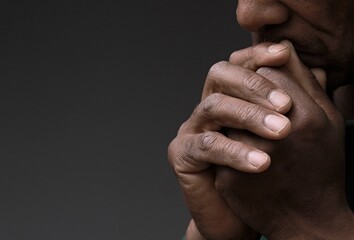 man praying to god with hands together Caribbean man praying with grey black background stock photo	