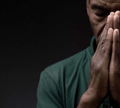 man praying to god with hands together Caribbean man praying with grey black background stock photo	