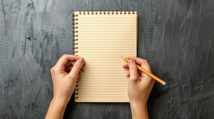 Obraz premium blank light brown notebook with lines, held by two hands and writing in notepad with pencil, gray background, top view.