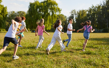 Group of a cute kids friends walking in the summer park. Happy girls and boys having fun and running outdoors. Smiling children in casual clothes spending time together on the lawn in nature.