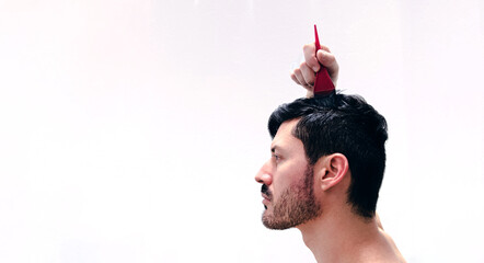 Hombre joven se tiñe el cabello con tinte natural de color castaño oscuro para cubrir sus canas. Tintura a base de henna. Vista de perfil con fondo blanco.  - obrazy, fototapety, plakaty