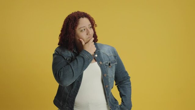 Pensive young woman 20s years old in denin jacket and white t-shirt posing looks around thinks scratches at temple comes up with ideas raised finger up isolated on yellow background in studio. People 