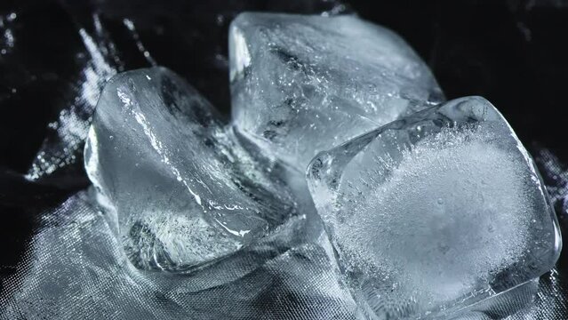 Ice cubes melting on a reflective shiny background, macro video, time lapse, dark contrast light.