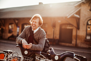 Mature man using a smart phone while picking up a bicycle from the public bicycle sharing station