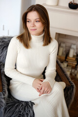 Beautiful fashionable young woman in elegant dress sitting in armchair at home