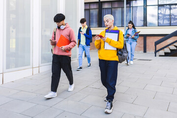 College students using mobile phone after classes while leaving university building campus.