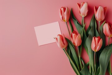 Pink flowers with a pink card on a pink background. The card is blank and the flowers are arranged in a vase