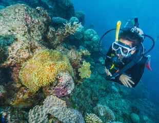 A woman is scuba diving in the ocean and is surrounded by coral