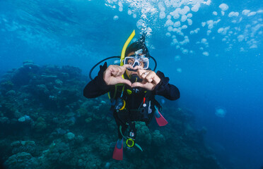 A woman is underwater with his hands together, making a heart shape