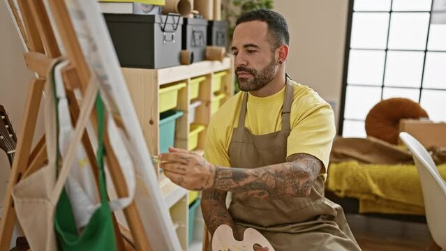 Bearded man painting on canvas in art studio wearing apron and smiling