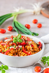 Pasta salad with pepper, tomatoes, spring onions and basil in a white bowl on light background, vertical