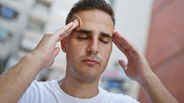 A young hispanic man in a white shirt appears stressed on a busy city street.