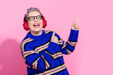 Photo portrait of lovely senior lady earphones point empty space wear trendy blue striped garment isolated on pink color background