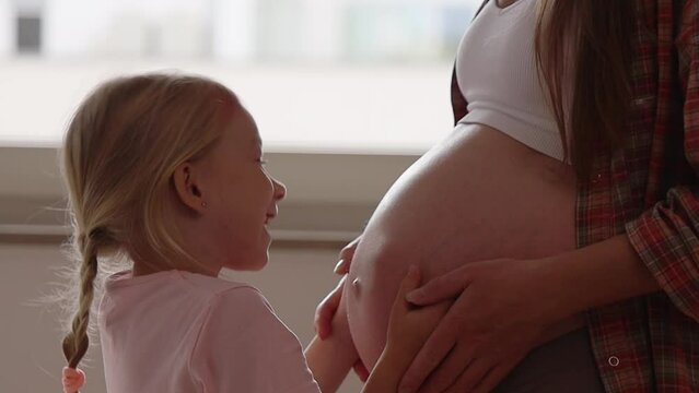 Preschool girl hugs pregnant mother.
