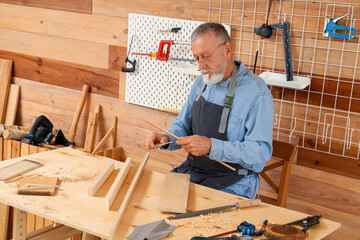 Mature carpenter working with wooden plank at table in shop