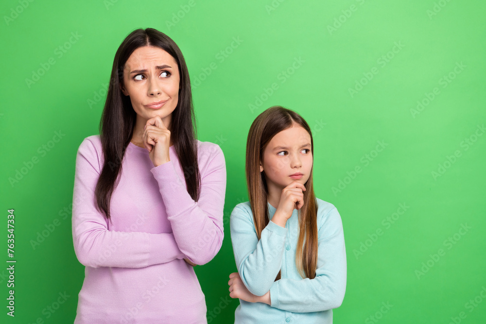 Poster Photo of suspicious unsure little girl mom dressed casual clothes arm chin looking empty space isolated green color background