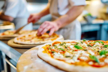 Deurstickers The chef in the pizzeria kitchen decorates a delicious pizza with mozzarella and basil © Виктория Марьенко