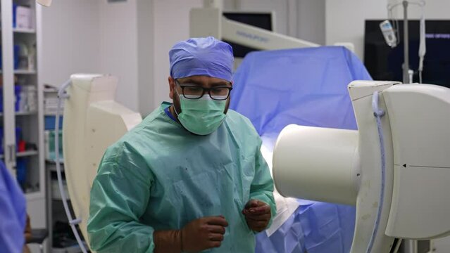 Rear view of a male surgeon standing near the operational table and C-Arm machine. Bearded doctor moves away from the equipment.