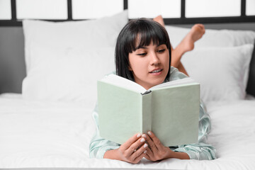 Young woman reading book on bed at home