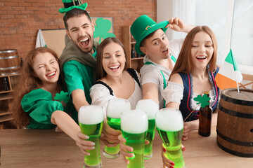 Group of young friends with beer celebrating St. Patrick's Day at table in pub