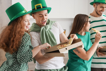 Group of young friends with pizza celebrating St. Patrick's Day in kitchen