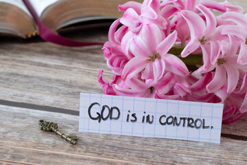 God is in control, handwritten quote with flower, ancient key, and open holy bible book on wood....