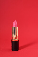 Pink lipstick in a black and gold tube on a red background with space for text. Vertical Photo