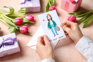 Female hands with kid drawing, gift boxes and tulips on beige grunge background. Happy Mother's Day