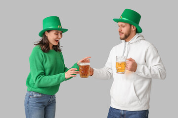 Beautiful young couple in leprechaun hats with glasses of beer on grey background. St. Patrick's Day celebration