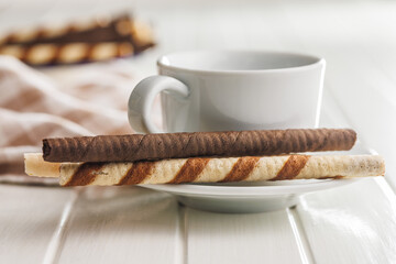 Assorted Chocolate and Vanilla Cream Filled Wafer rolls and coffee cup on white table.