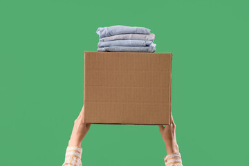 Woman with moving box and folded clothes on green background
