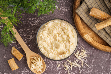 Horseradish sauce in bowl and spoon with ground horseradish on grey background. Top view