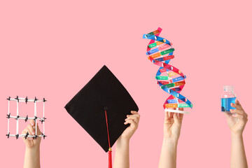 Female hands holding molecular model with graduation hat, DNA model and filled bottle on pink...