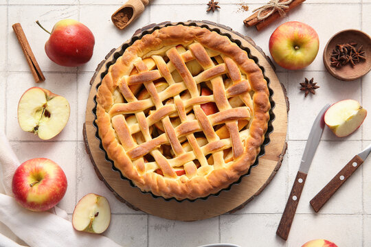 Tasty homemade apple pie with fruits, cinnamon and cutlery on white tile background