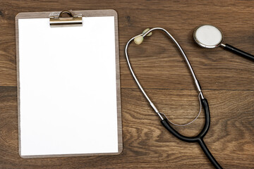 Blank medical clipboard with stethoscope on wooden table