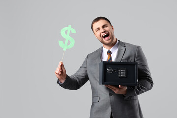 Happy young man with safe box and paper dollar sign on grey background