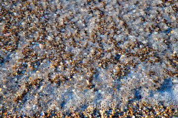 Seafoam from waves over beached pebbles