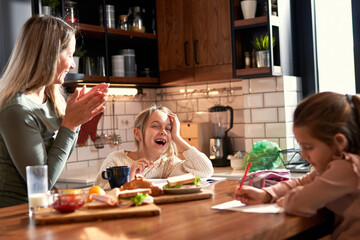 Mother and two daughters share the kitchen table, with mom and the elder sister working on homework...