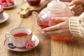 Young woman holding teapot with hibiscus tea in kitchen