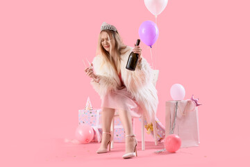 Young woman with hangover and champagne sitting after Birthday party on pink background