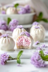 Obraz na płótnie Canvas White chocolate sweets with pink icing inside and delicate purple flowers. Rounded sweets of white chocolate and soft shape on a marble countertop.