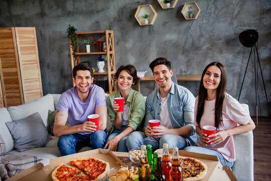 Photo of company positive funky friends sitting couch hold plastic beer cups eat pizza loft interior house inside