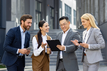 A professional business team in formal attire engaged in a discussion outside a modern office building.