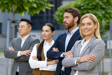 A group of four diverse business professionals confidently standing lined up outside an office building, portraying teamwork and leadership.
