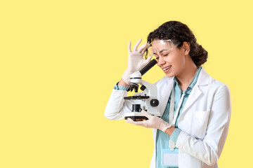 Female African-American chemist with microscope on yellow background