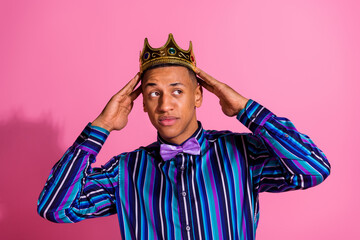 Photo of doubtful unsure guy dressed striped shirt golden tiara looking empty space isolated pink color background