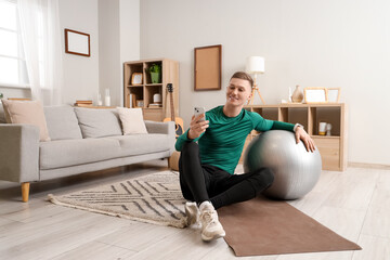 Sporty young man with fitball using mobile phone at home