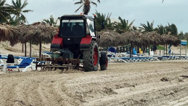 Varadero, December - 2023. Tractor on the beach of the Atlantic Ocean. A tractor cleans the sand on a Cuban beach. A tractor cleans the beach sand from algae. Cleaning the coast at the resort. 4К