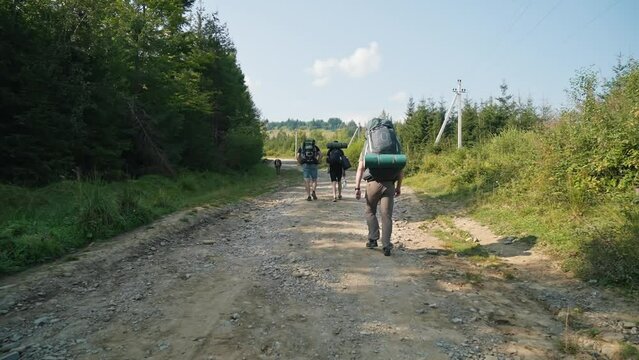 A group of tourists with backpacks climbs the mountain on a dirt road. Mountain climbing, nature, good natural conditions in the mountains.