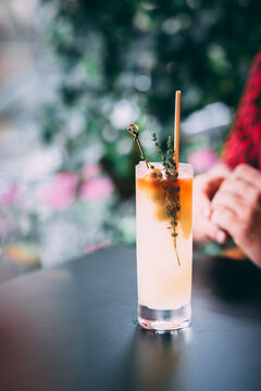 A man in a red shirt holds a classic gin cocktail garnished with orange fruit, against a background of summer flowers. Bright light adds to the atmosphere of celebration and enjoyment.